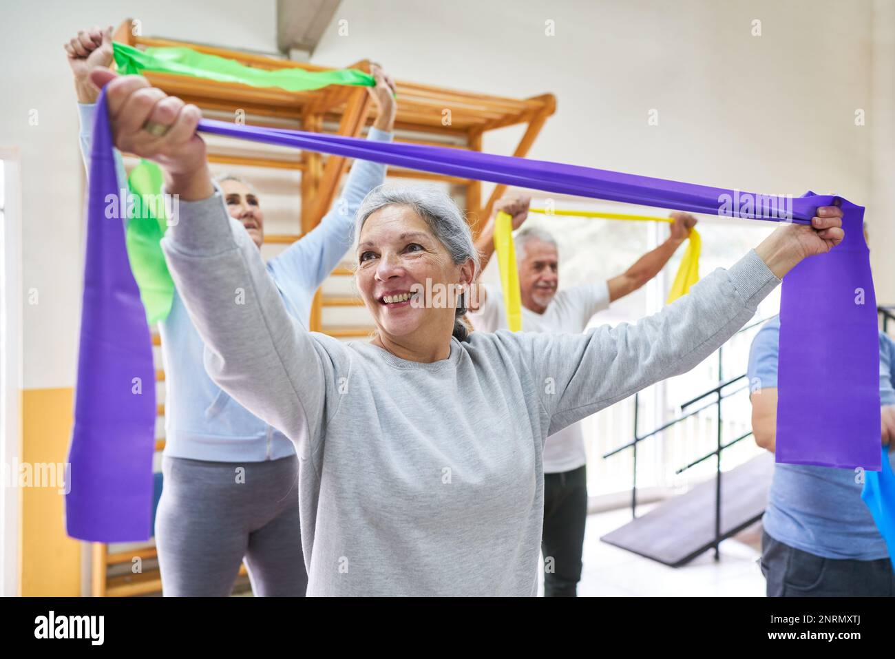 Femme et hommes âgés souriants faisant de l'exercice avec des bandes élastiques au centre de réadaptation Banque D'Images