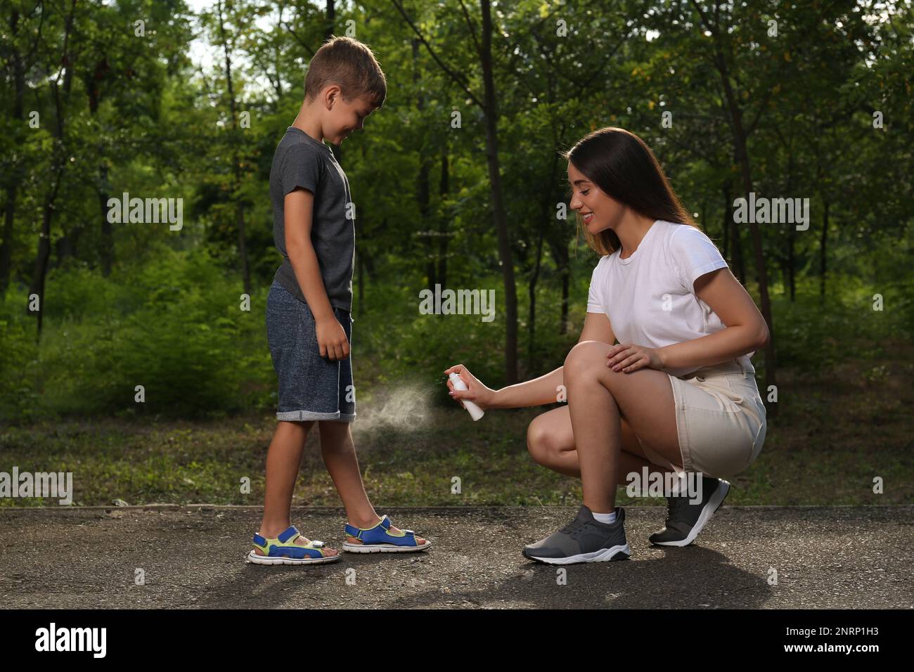 Femme appliquant un insectifuge sur la jambe de son fils dans le parc. Prévention des piqûres de tiques Banque D'Images