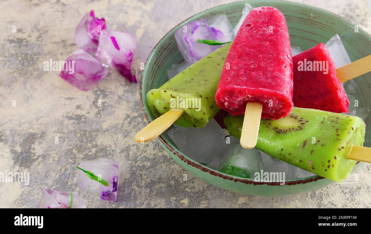 Glace à la kiwi et à la framboise maison ou popsicles avec fleurs congelées  sur table en béton, jus de fruits congelés, style vintage, carré Photo  Stock - Alamy