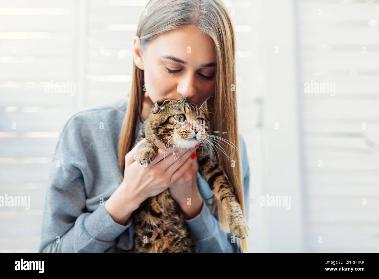 Jolie jeune femme Blonde tient un chat écossais à l'œil vert mignon dans ses bras et l'embrasse à l'extérieur, concept d'aimer et de prendre soin des animaux de compagnie Banque D'Images