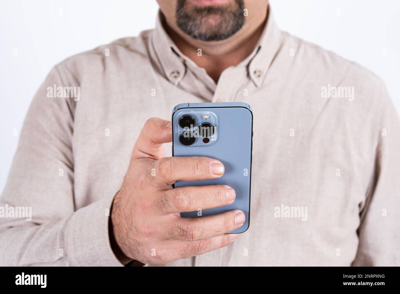 Image rognée d'un homme à l'aide d'un smartphone moderne. Téléphone mobile bleu avec trois caméras. Isolé sur fond blanc. Tenir le téléphone portable d'une main. Banque D'Images