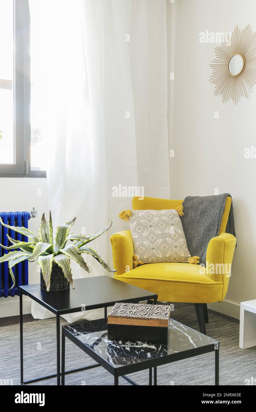 Coin d'un appartement décoré d'un fauteuil jaune avec des tables basses en métal noir et un avec un dessus en marbre noir poli Banque D'Images