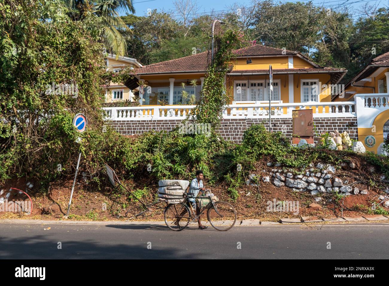 Panjim, Goa, Inde - janvier 2023 : un Indien marchant avec son vélo devant une ancienne grande maison portugaise de l'époque dans le quartier d'Altinho à Panaji. Banque D'Images