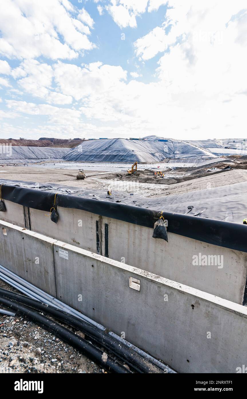 Ponceau en béton au premier plan avec une géomembrane couvrant et stabilisant des monticules de sol excavé en arrière-plan dans une décharge active. Banque D'Images