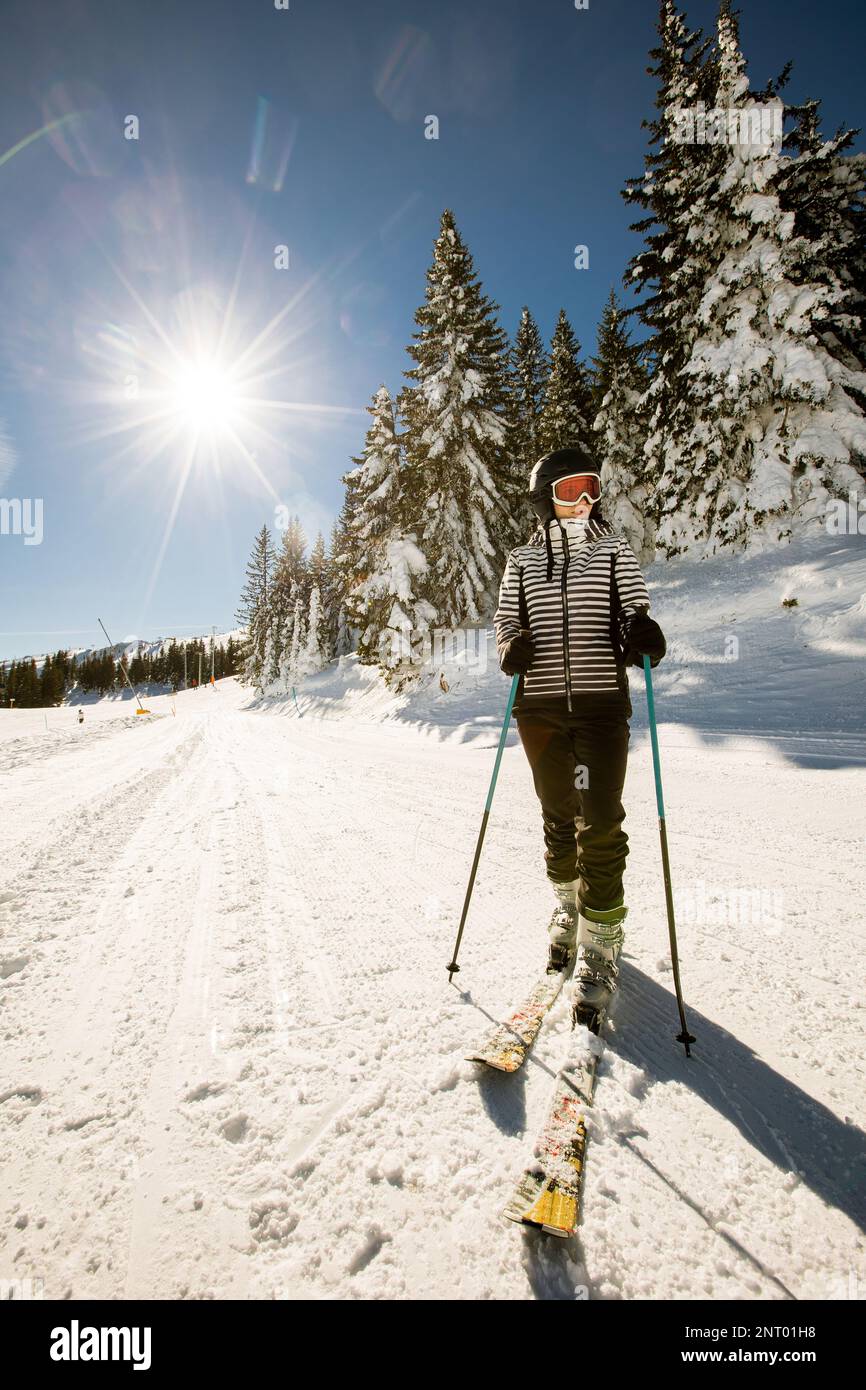 Jeune femme qui profite de la journée d'hiver pour skier sur les pistes enneigées, entourée de grands arbres et habillée pour les températures froides Banque D'Images