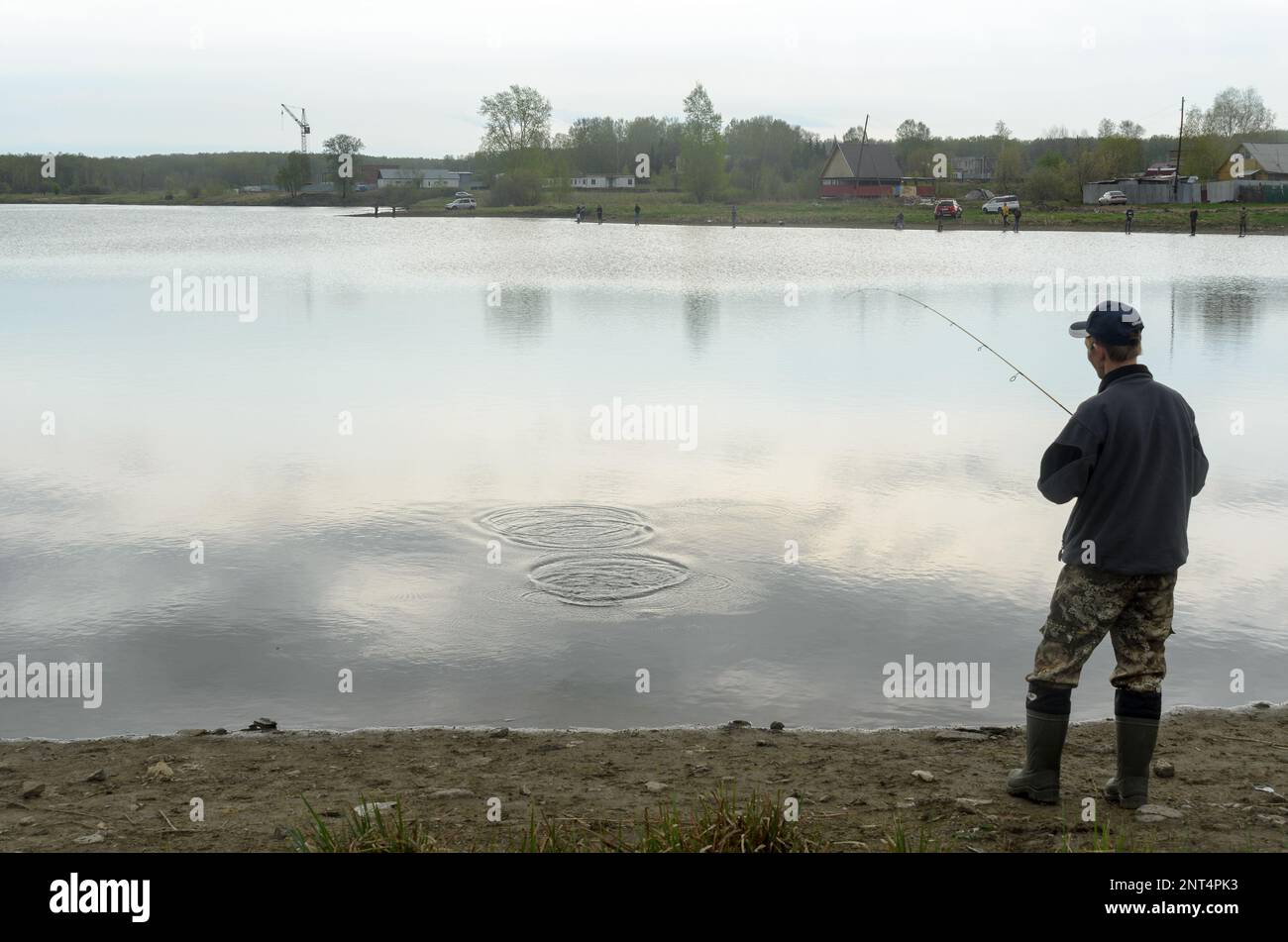 Le pêcheur russe moderne de sexe masculin pêche sur une tige de rotation ultra-légère dans la pluie sur un lac en Sibérie. Banque D'Images