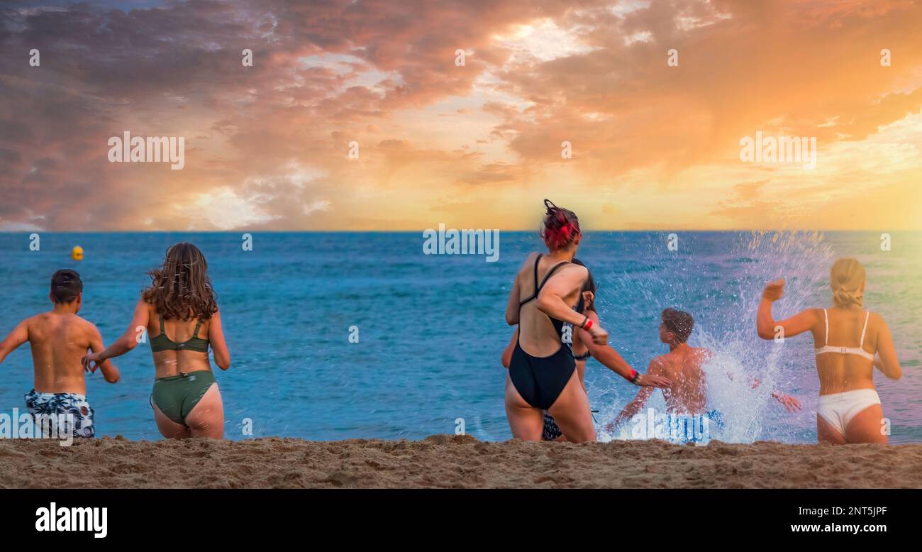 Jeunes amis qui courent dans la mer au coucher du soleil à Bournemouth, Angleterre Banque D'Images