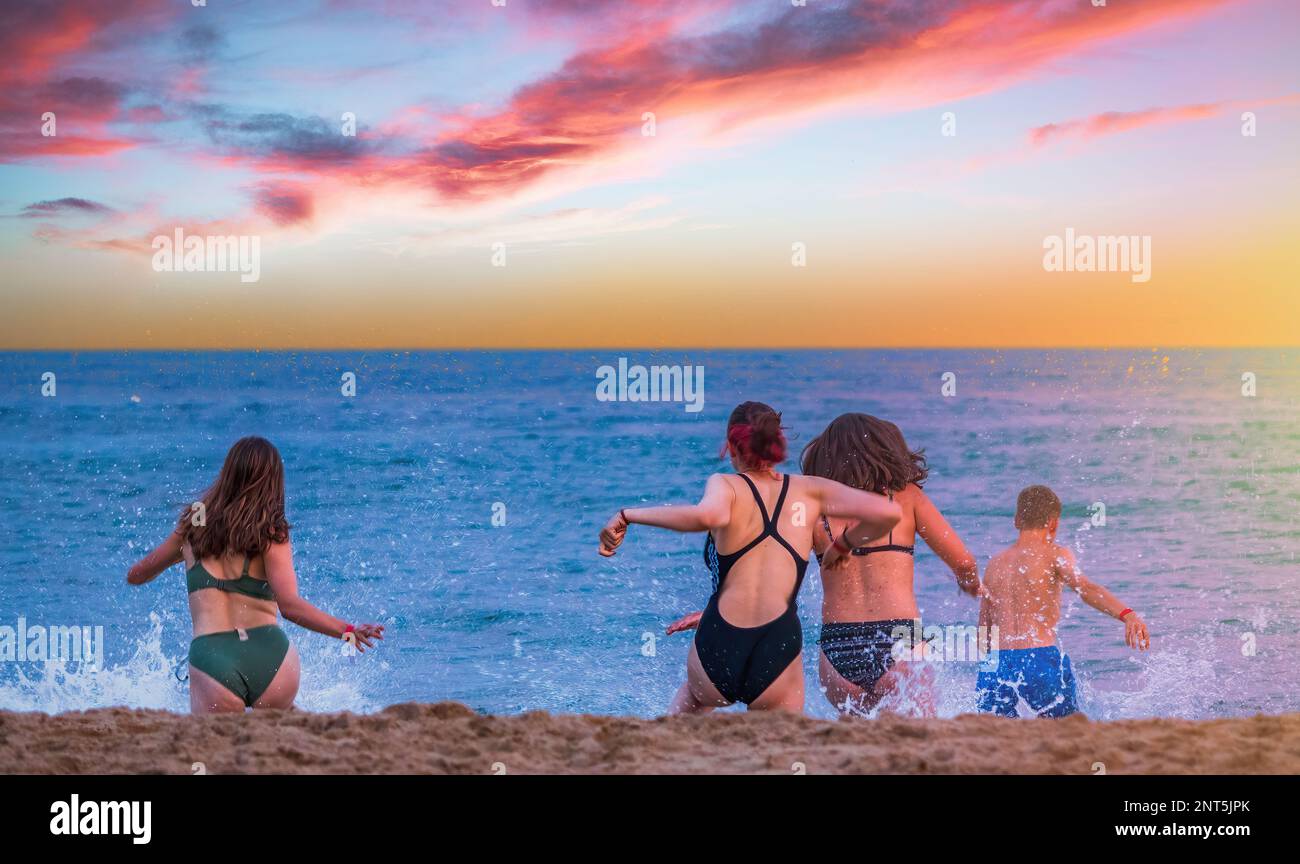 Jeunes amis qui courent dans la mer au coucher du soleil à Bournemouth, Angleterre Banque D'Images