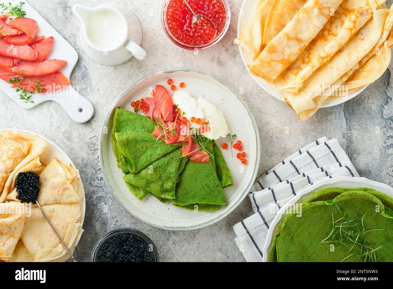 Assortiment de crêpes vertes et blanches. Fines crêpes d'épinards verts et de crêpe blanche avec caviar rouge et noir, sauce sur fond de table en béton gris Banque D'Images