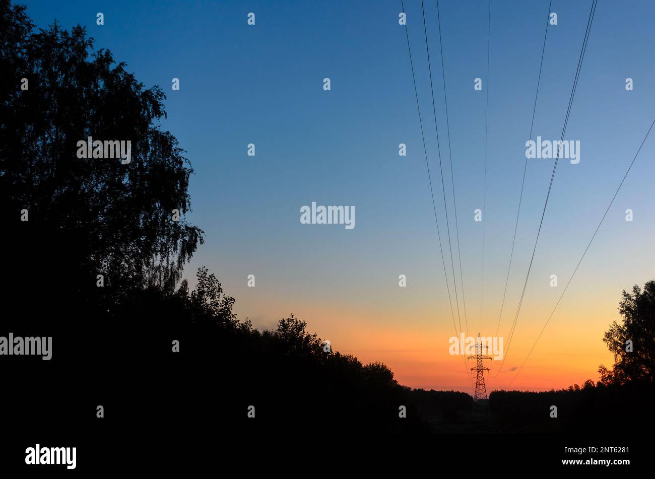 Le support d'ancrage d'extrémité des lignes électriques aériennes avec des fils est à l'horizon sur un beau gradient de ciel de coucher de soleil orange vif sur la forêt sombre, à travers le Banque D'Images