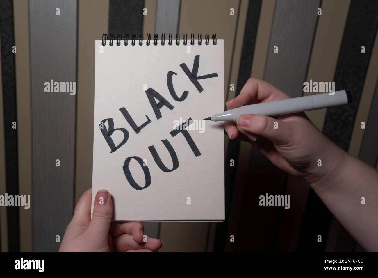 Une fille dans une pièce sombre tient un carnet avec l'inscription « Blackout » dans une main et un stylo dans l'autre main (gros plan). Concept de coupure de courant. Crise énergétique Banque D'Images