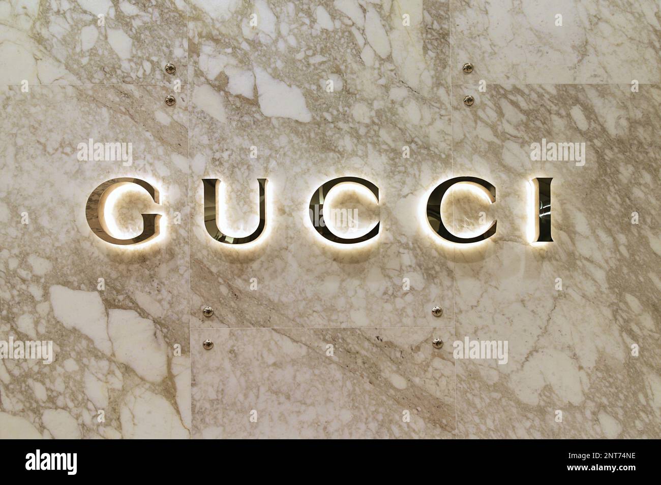 Logo Gucci doré rétroéclairé sur un mur en marbre Havane Banque D'Images
