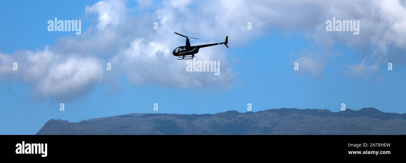 Vue panoramique d'un Robinson R44 Raven II noir revenant à son héliport de l'île de la Réunion. Banque D'Images