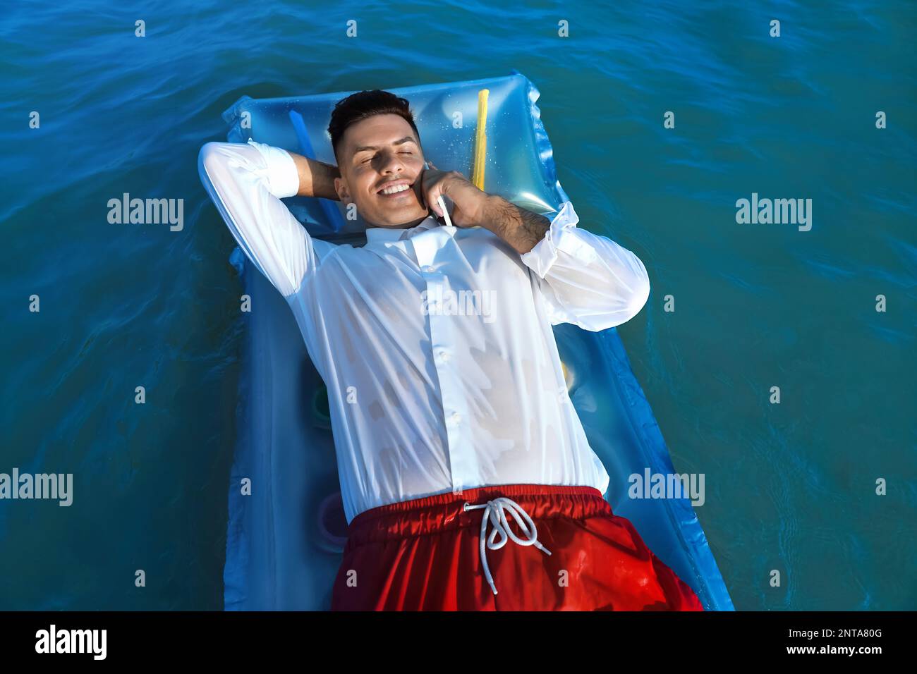 Homme heureux parlant par téléphone portable tout en flottant sur un matelas en mer. Voyage d'affaires Banque D'Images