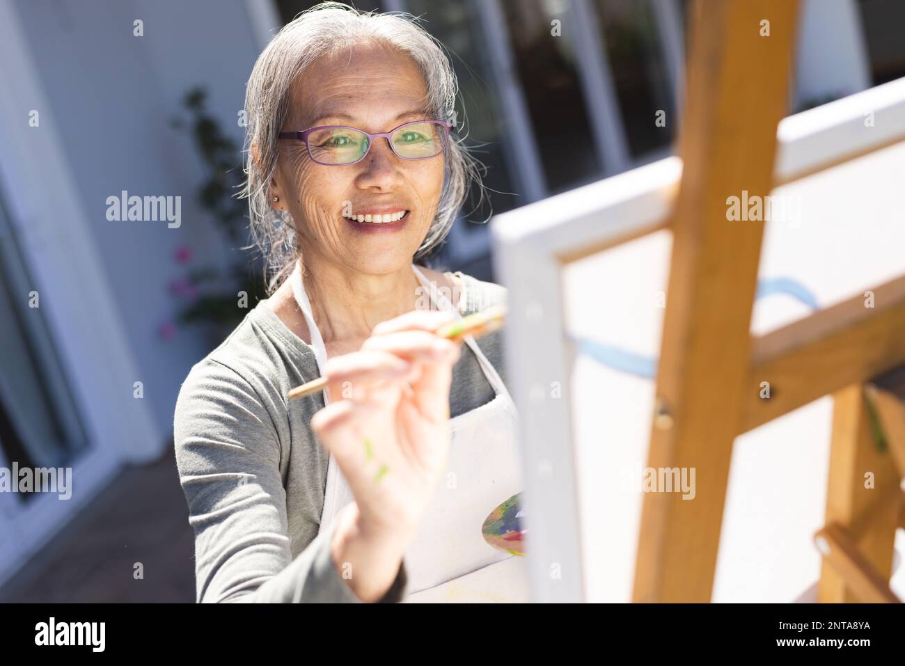 Bonne femme asiatique senior peignant sur un chevalet dans le jardin Banque D'Images