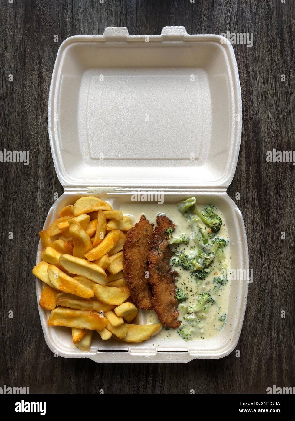 L'allemand de la nourriture à emporter : schnitzel (escalope panée) avec frites et sauce au fromage dans le brocoli en polystyrène sur table en bois rustique Banque D'Images