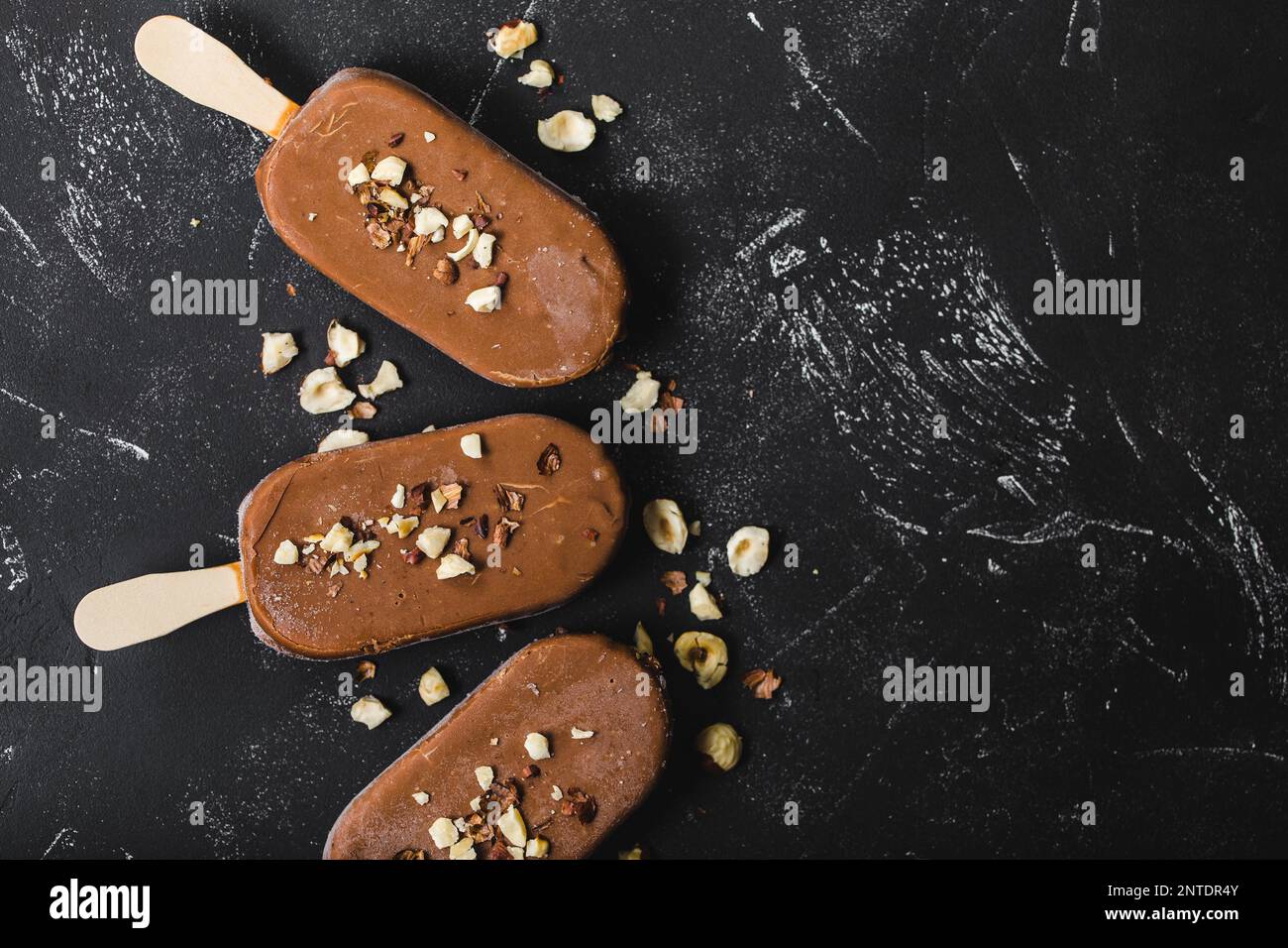 Pop-sutes au chocolat au lait et aux noisettes. Gros plan. Glaces à la crème, papillotes recouvertes de chocolat, bâtonnets, fond en marbre de pierre noire. Espace pour le texte. Banque D'Images