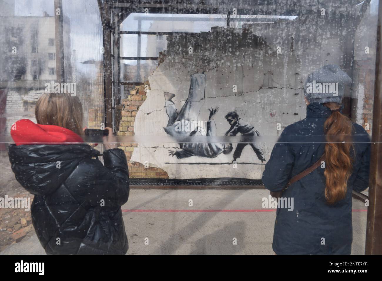Borodyanka, Ukraine. 26th févr. 2023. Une femme prend des photos du travail de Banksy avec son téléphone, le travail de l'artiste anglais Banksy est visible sur le mur détruit, après que la Fédération de Russie a attaqué la ville de Borodyanka, les autorités ont décidé de sauver le travail de Banksy et maintenant ils sont protégés par le système. Crédit : SOPA Images Limited/Alamy Live News Banque D'Images