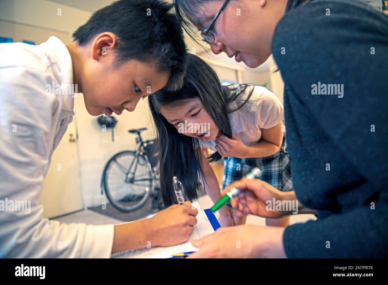 Vivian Loh, center, a seventh grader at Winchester Thurston School and the first girl to win the Pennsylvania MATHCOUNTS competition, explains the solution to a math problem to her brother Vincent, 10, and their mother Debbie after they each completed a practice worksheet in the morning before school, Thursday, April 25, 2019, at their home in Squirrel Hill. (Alexandra Wimley/Pittsburgh Post-Gazette via AP) Banque D'Images