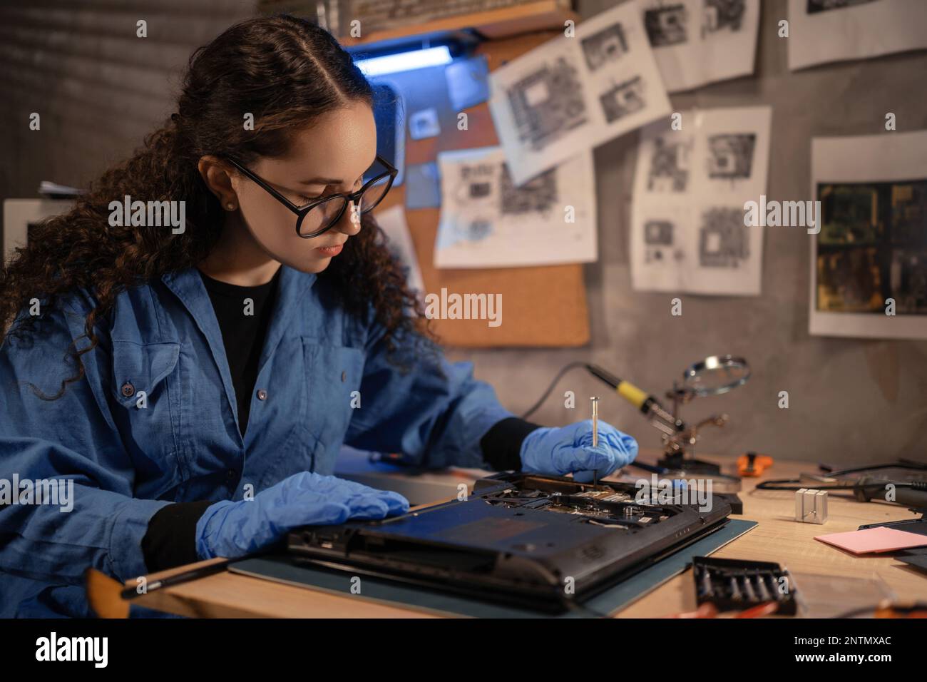 Une femme technique réparant une carte mère d'ordinateur cassée dans un atelier. Démontage de l'ordinateur portable avec un tournevis dans un ancien atelier de réparation. Rénovation électronique, techn Banque D'Images