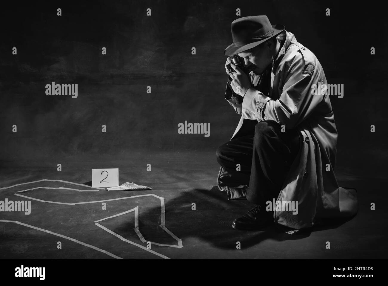 Noir et blanc, noir. Homme, détective en chapeau et en trench-coat regardant sur la silhouette humaine dessinée sur le sol et prenant des photos Banque D'Images
