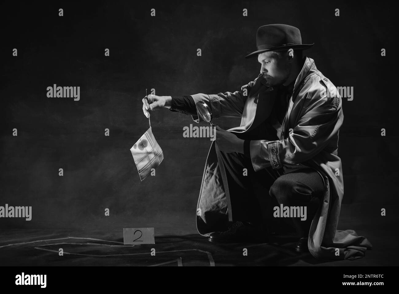 Noir et blanc, noir. Homme, détective assis près de la silhouette humaine dessinée sur le sol regardant le mouchoir avec des taches de sang dans la loupe Banque D'Images