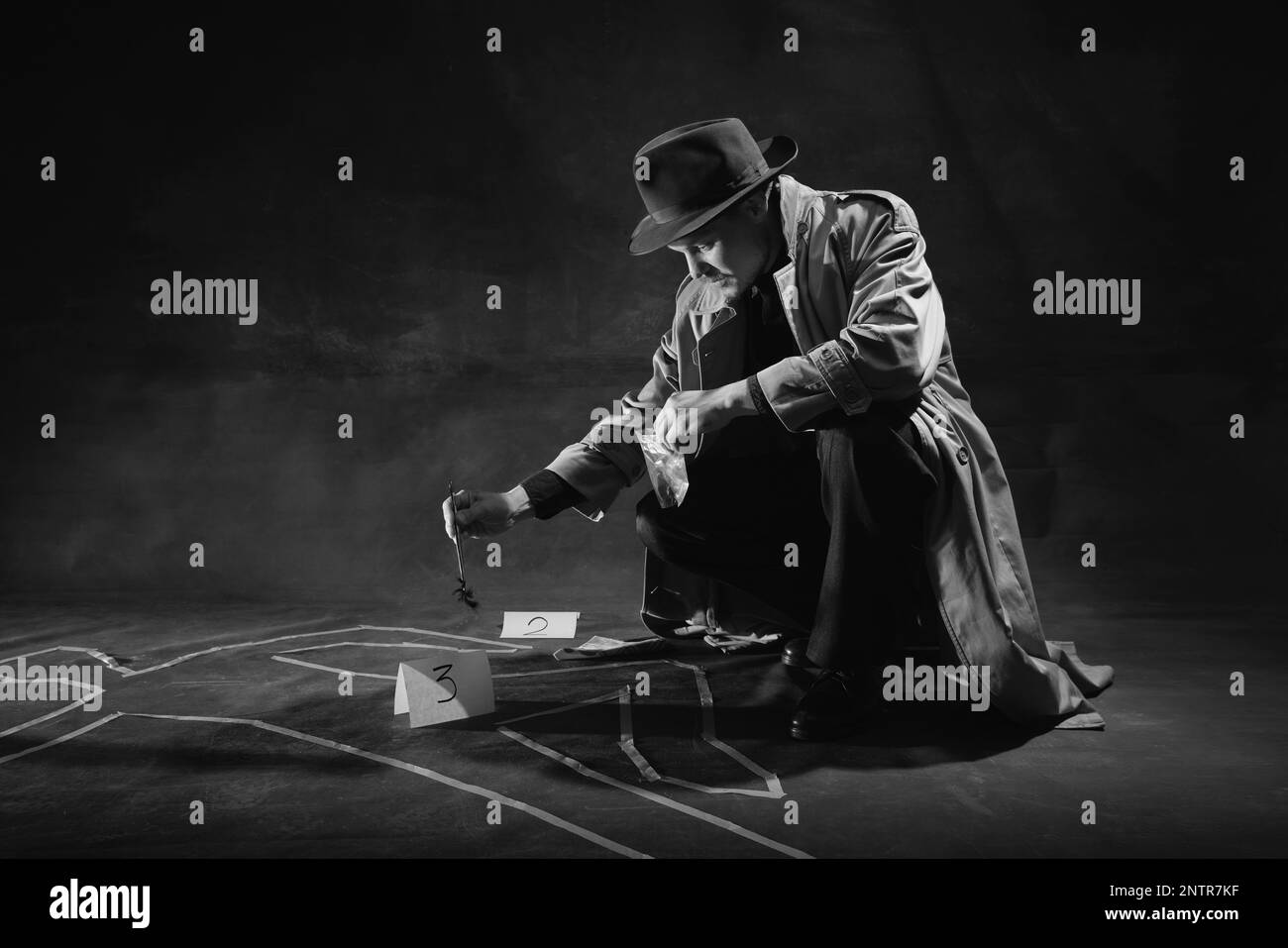 Noir et blanc, noir. Homme, détective en chapeau et trench-coat près de la silhouette humaine dessinée sur le sol, ramasser des indices Banque D'Images