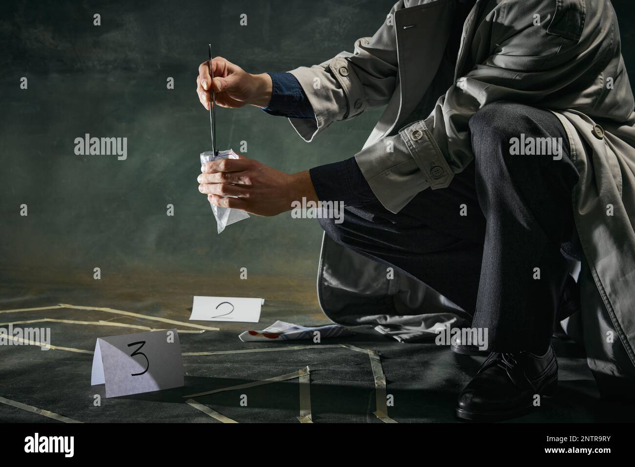 Image rognée de l'homme détective en trench coat ramassant l'enquête indice sur fond vert foncé vintage. Crime Banque D'Images