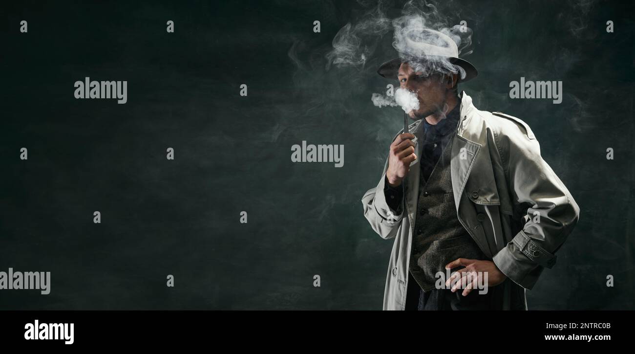 Portrait de l'homme, détective en trench coat et chapeau fumant pipe sur fond vert foncé vintage. Bannière Banque D'Images