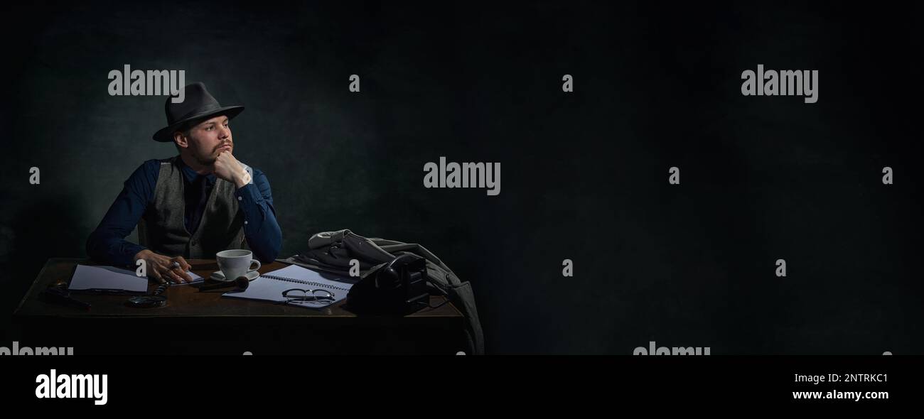 Détective professionnel en chapeau fedora assis à table avec une expression sérieuse et réfléchie sur fond vert foncé vintage. Bannière Banque D'Images
