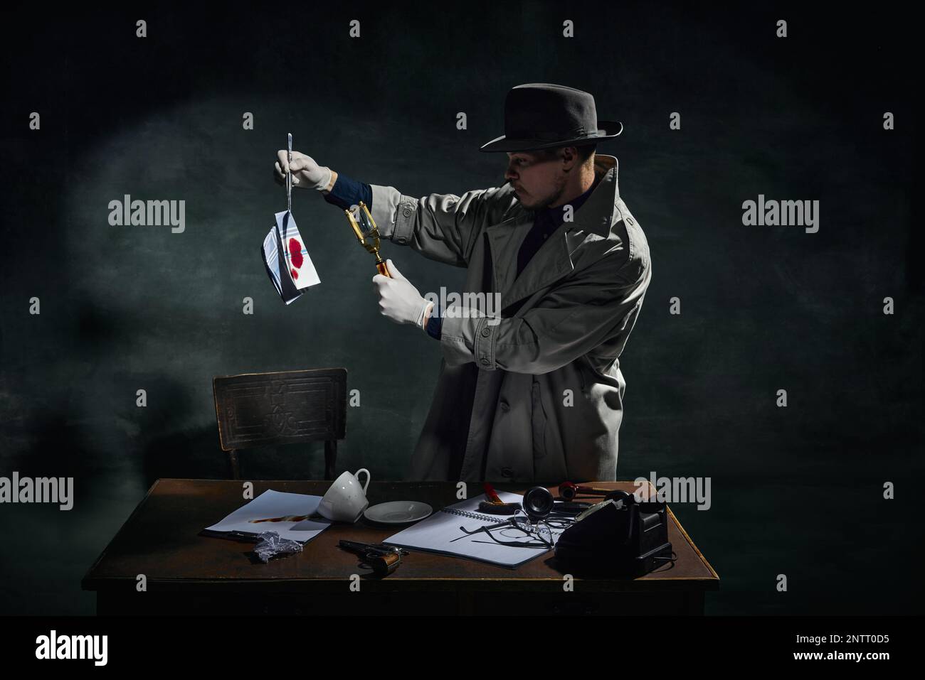 Détective professionnel en trench-coat regardant dans la loupe sur le mouchoir avec des taches de sang sur fond vert foncé vintage Banque D'Images