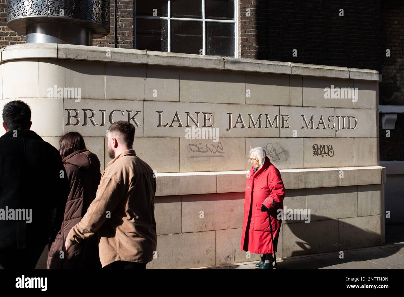 Les gens qui marchent devant une inscription à la mosquée de Brick Lane Jamme Masjid sur Brick Lane, à l'est de Londres. Ombres à contraste élevé. Banque D'Images