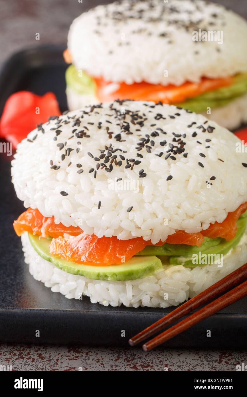 Hamburger à sushi à l'avocat et au saumon au sésame noir et au gingembre, sur une assiette sur la table. Verticale Banque D'Images