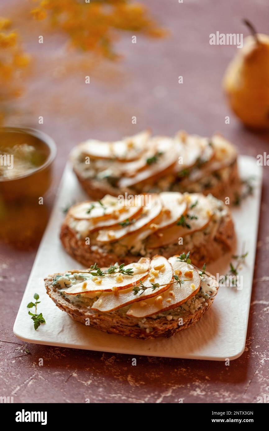 roquefort de fromage français et de tranches de pêches toasts sur une assiette carrée, sur une table sous des fleurs mimosa Banque D'Images