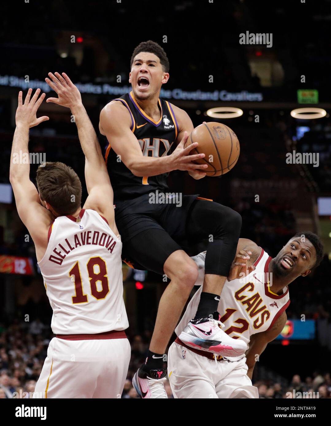 Phoenix Suns' Devin Booker, center, drives to the basket between Cleveland Cavaliers' Matthew Dellavedova, left, and David Nwaba in the second half of an NBA basketball game, Thursday, Feb. 21, 2019, in Cleveland. (AP Photo/Tony Dejak) Banque D'Images