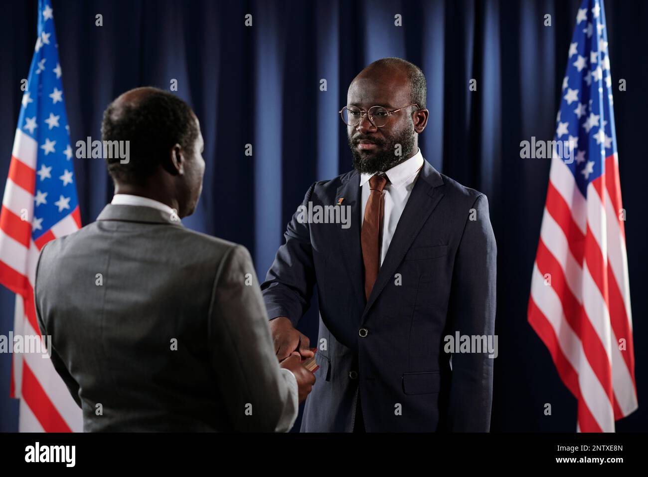 Nouveau président des États-Unis gardant la main droite sur la Sainte Bible pendant le serment de bureau tout en se tenant devant un homme afro-américain mature Banque D'Images