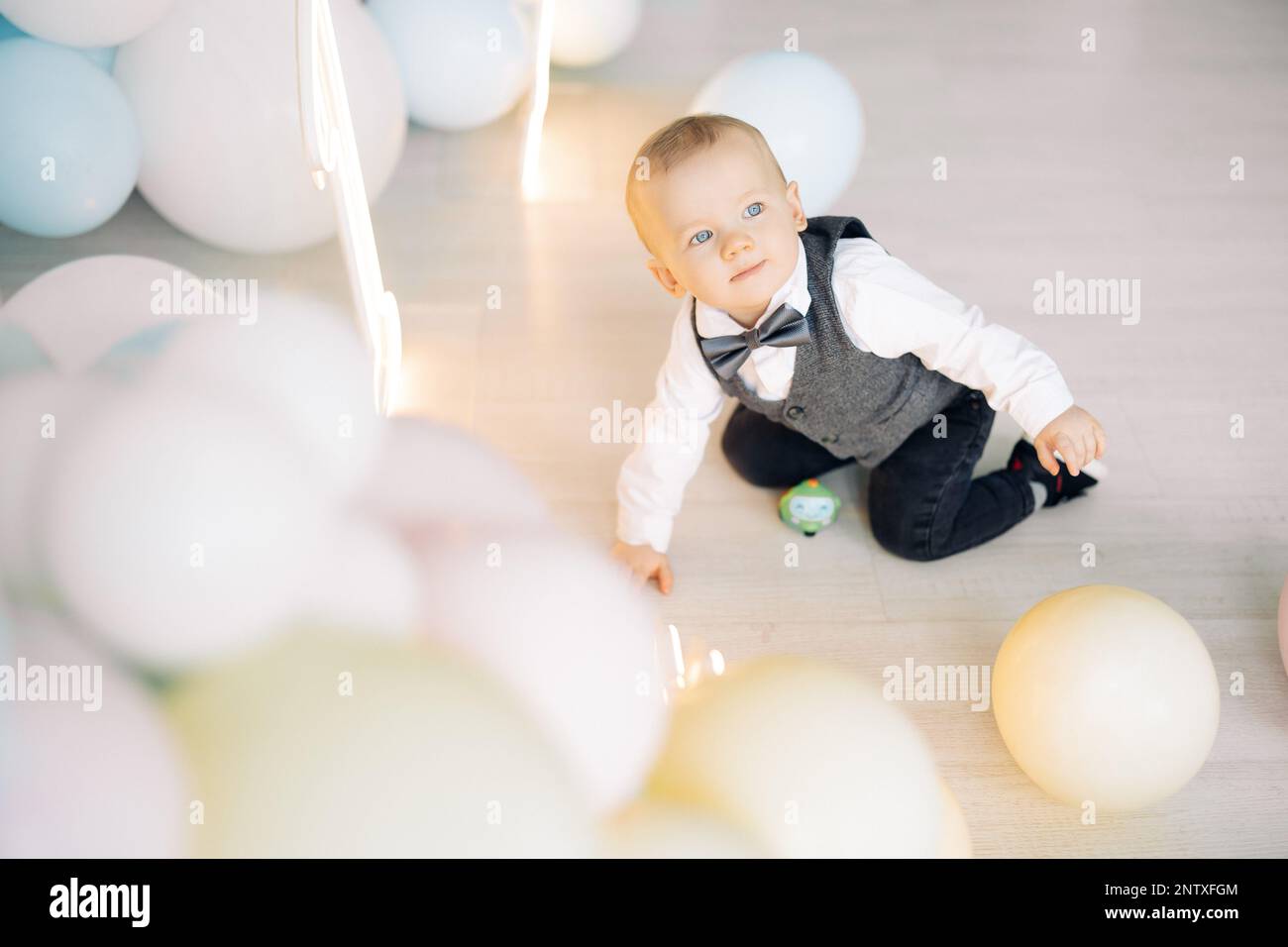 Un garçon d'un an est rampant sur le sol parmi beaucoup de ballons colorés et un chiffre derrière lui. Célébration du premier anniversaire. Événement festif. Banque D'Images