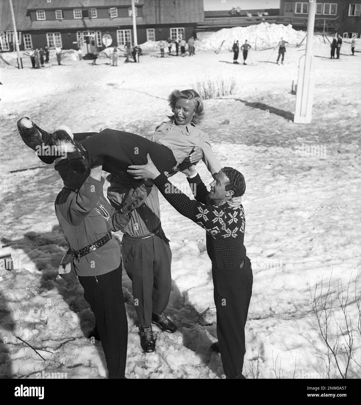 Dans les montagnes enneigées 1940s. Olga Sjögren, de Stockholm, est habillée de la mode sportive d'hiver typique de 1940s, qui a été jetée dans les airs par trois hommes célébrant sa réalisation, grimpant la montagne Kuoblatjåkko à Norrbotten en Suède. La dernière des sept montagnes qu'elle a grimpé pour recevoir le prix: Les sept pics. Elle a passé 60 heures et a grimpé de 6558 mètres au total après avoir terminé. Suède 1943 Kristoffersson réf. H138-2 Banque D'Images