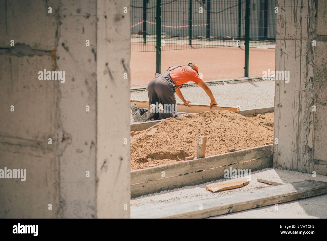 Un travailleur inconnu utilise un morceau de bois et un plancher redressant de sable et de gravier pour le préparer à la couche d'asphalte. Banque D'Images