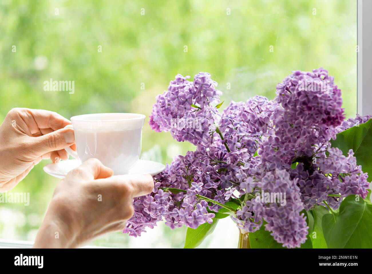 Intérieur avec un bouquet de fleurs de lilas sur la fenêtre. Thé le matin du printemps dans la cuisine près de la fenêtre Banque D'Images