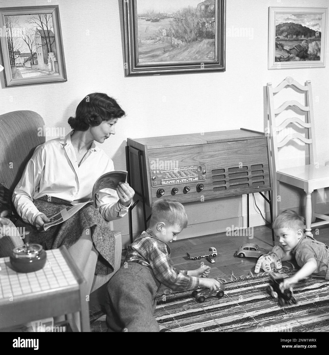 Une femme au foyer et une mère avec ses deux garçons devant la radio. Gramophone radio typique de 1957. Un gramophone radio qui a donné l'occasion d'écouter la radio et de lire des enregistrements gramophones dans la même unité. Suède 1957. Réf. BV19-8 Banque D'Images