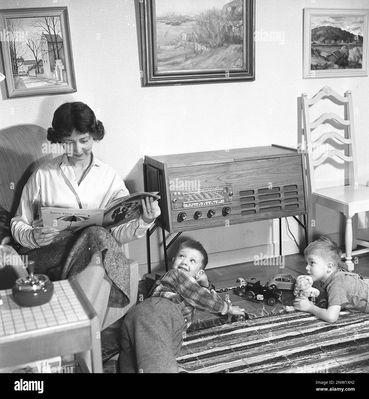 Une femme au foyer et une mère avec ses deux garçons devant la radio. Gramophone radio typique de 1957. Un gramophone radio qui a donné l'occasion d'écouter la radio et de lire des enregistrements gramophones dans la même unité. Suède 1957. Réf. BV19-12 Banque D'Images
