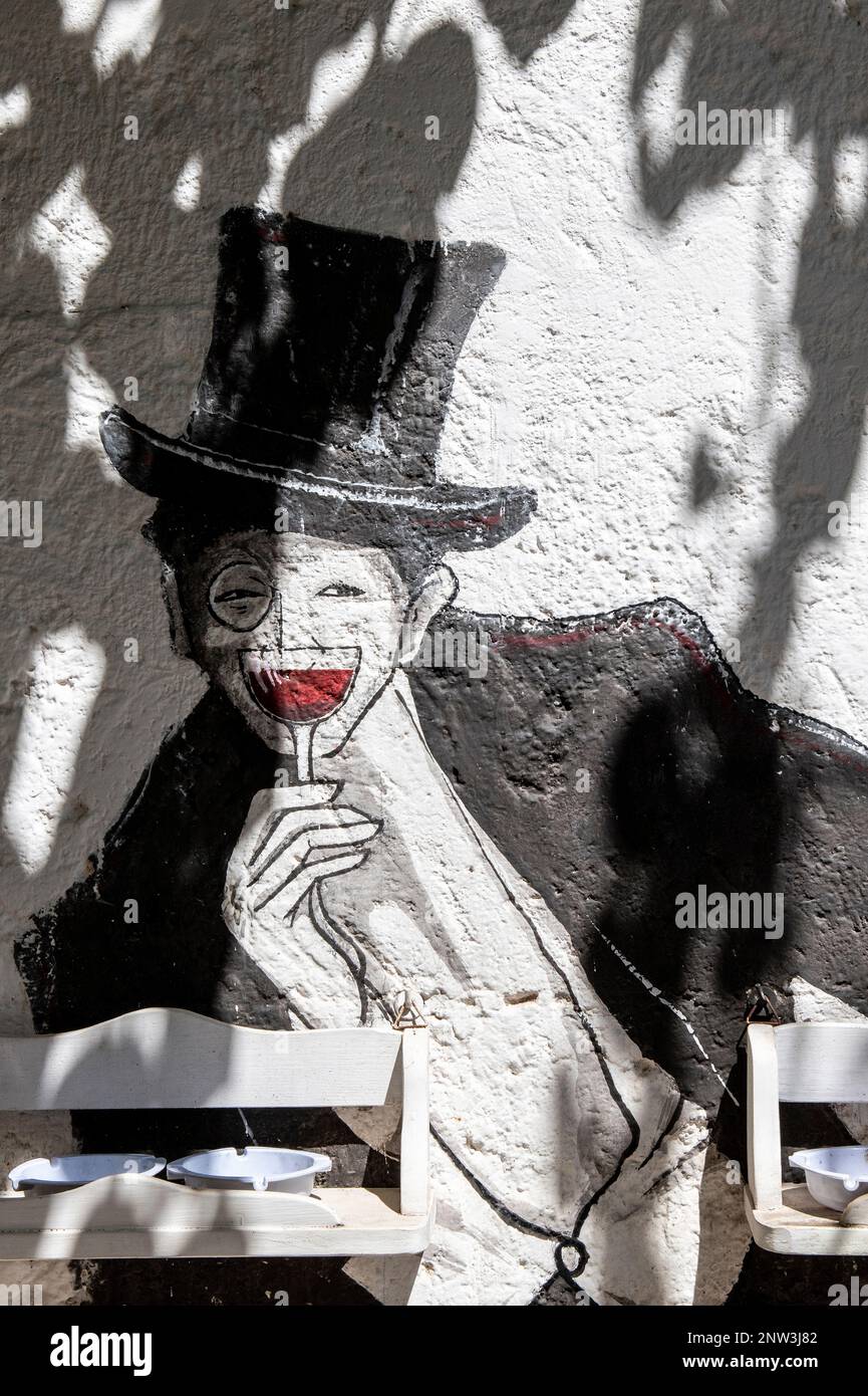 Art de rue d'un homme avec un chapeau de haut tenant un verre d'un vin rouge dans une rue paisible de Grottaglie, Puglia, Italie Banque D'Images