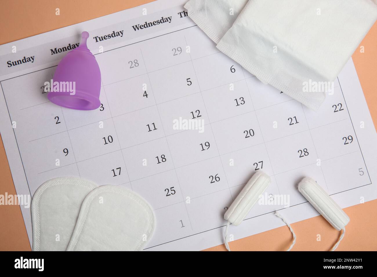 Composition Flat Lay avec calendrier et blocs menstruels sur fond orange pâle Banque D'Images