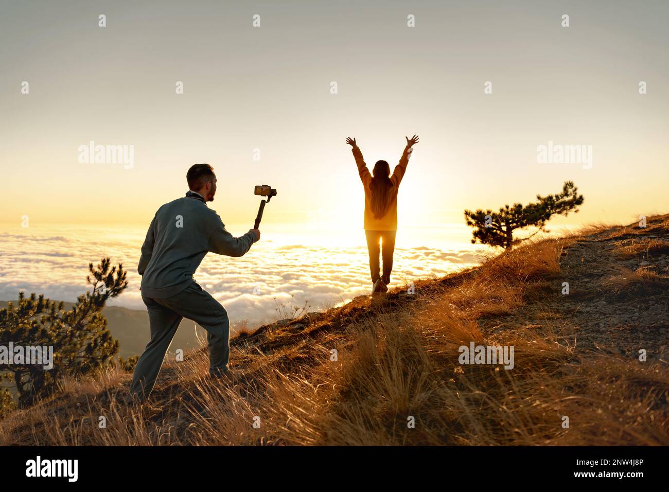 Homme touriste avec stabilisateur électronique gimbal prend la vidéo de tournage avec la fille heureuse au lever du soleil sommet de montagne Banque D'Images