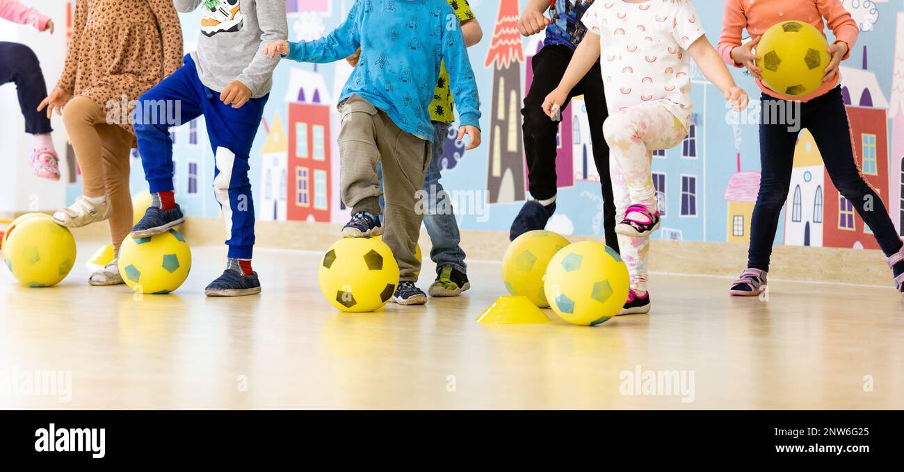 Enfants de la maternelle à la classe de football. Groupe d'enfants avec des ballons de football en mousse debout dans la ligne et des balles de coups de pied. Entraînement de football sportif à Banque D'Images