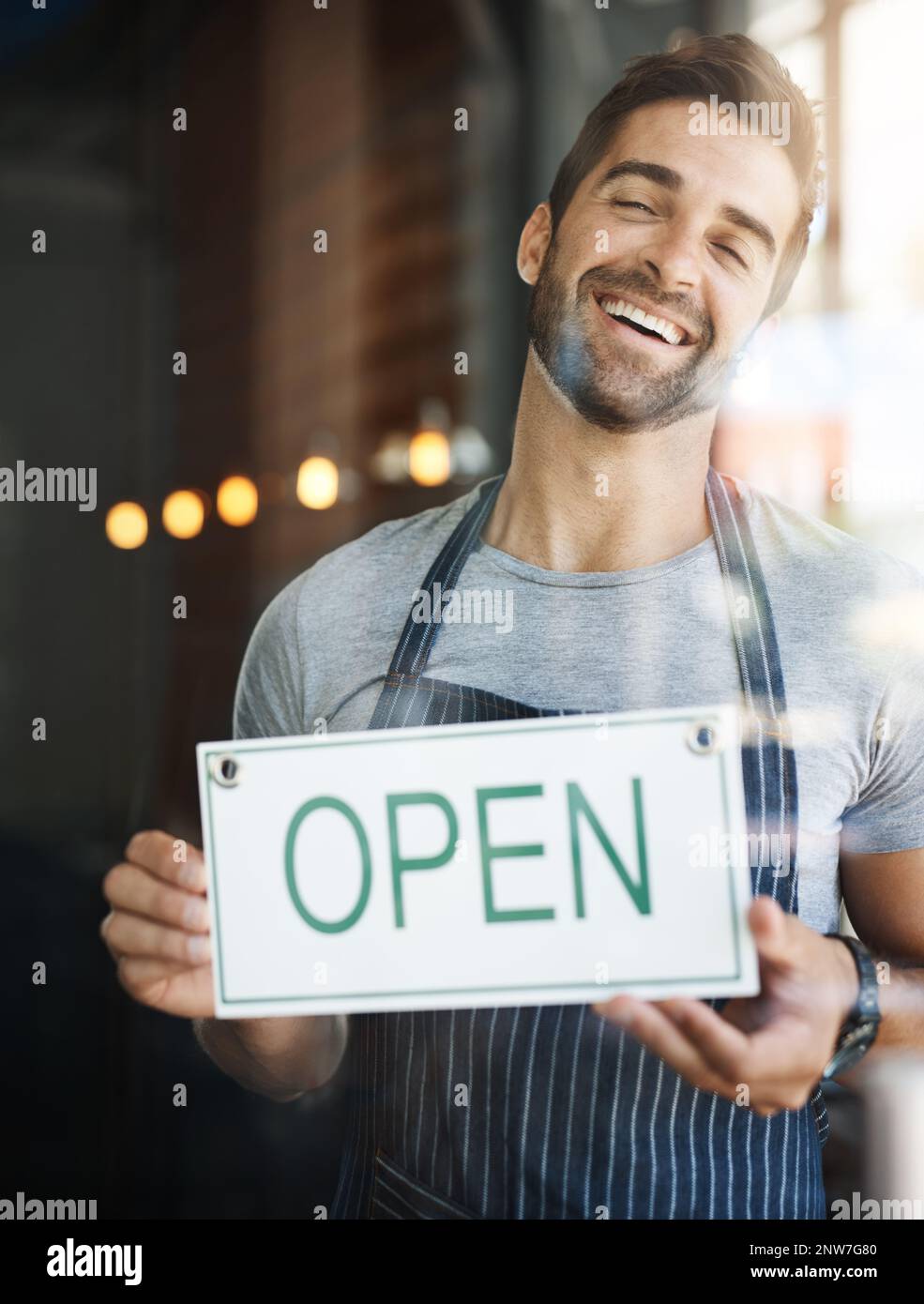 Nous allons vous préparer un café. Photo d'un beau jeune homme qui pendait une affiche ouverte sur la porte de son magasin. Banque D'Images