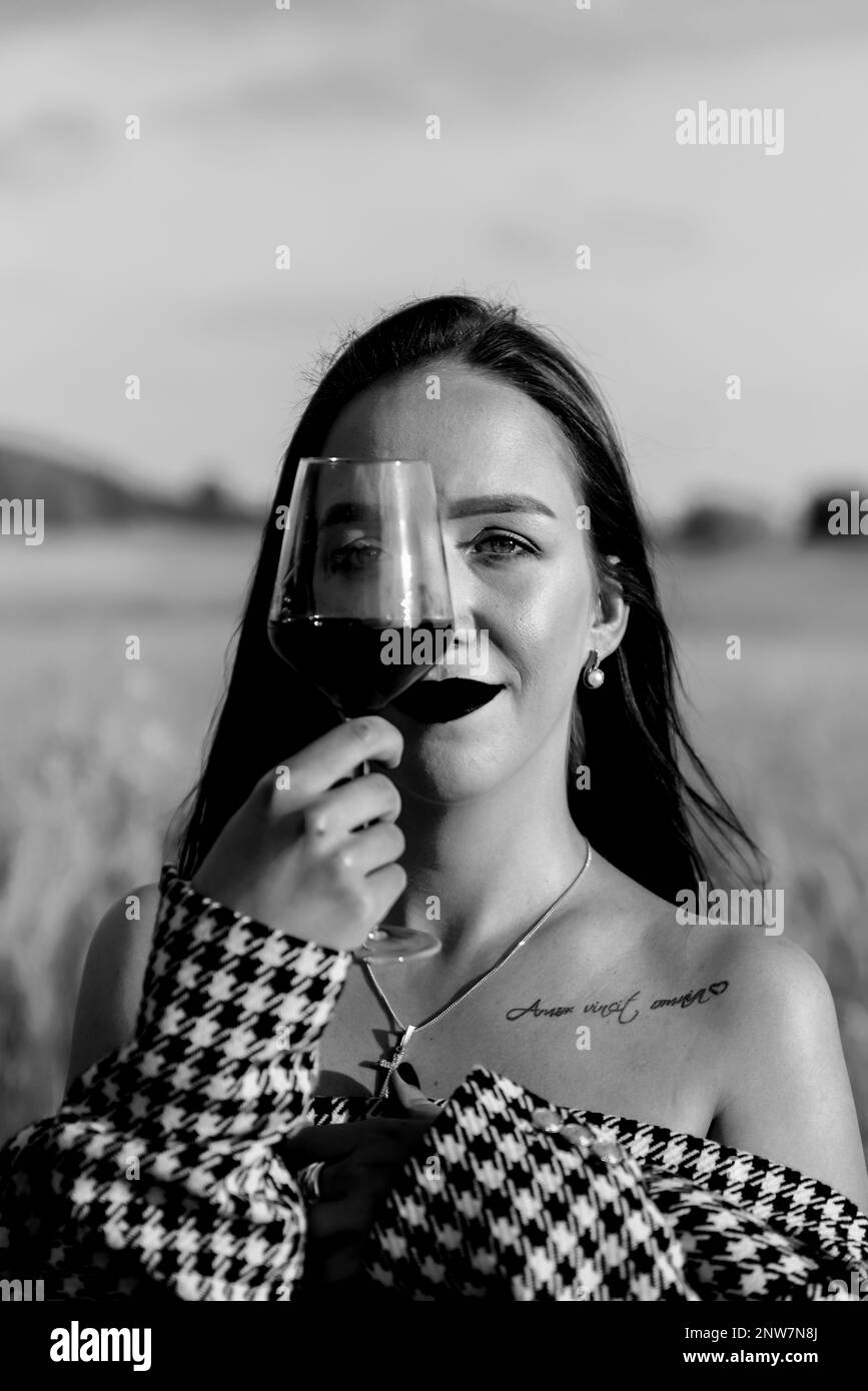 Jeune femme avec un verre de vin rouge sur champ de blé en noir et blanc Banque D'Images