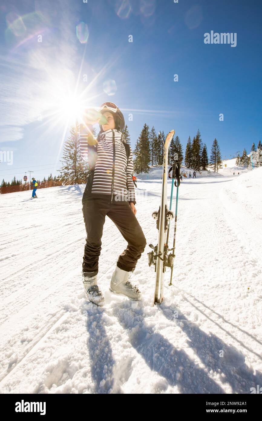 Jeune femme qui profite de la journée d'hiver pour skier sur les pistes enneigées, entourée de grands arbres et habillée pour les températures froides Banque D'Images