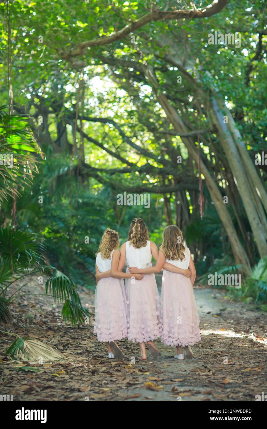 trois sœurs dans des robes rose pâle marchant à travers le tunnel des arbres bras dans le bras Banque D'Images
